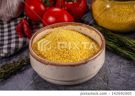 Yellow couscous in speckled ceramic bowl surrounded by fresh tomatoes, garlic, red chili peppers, rosemary and thyme on dark textured surface Yellow couscous in speckled ceramic bowl surrounded by fresh tomatoes, garlic, red chili peppers, rosemary and thyme on dark textured surface 142692805