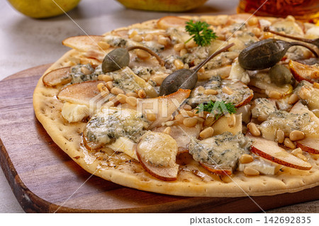 Gourmet pear and blue cheese flatbread with pine nuts and olives on wooden board Gourmet pear and blue cheese flatbread with pine nuts and olives on wooden board 142692835