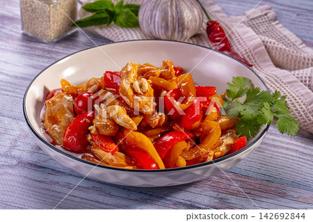 Stir-fried chicken with red and yellow bell peppers in glossy sauce, garnished with cilantro, served in white bowl on rustic wooden table Stir-fried chicken with red and yellow bell peppers in glossy sauce, garnished with cilantro, served in white bowl on rustic wooden table 142692844
