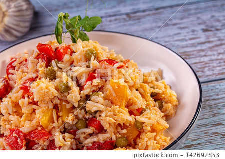 Fried basmati rice with red bell peppers, green peas, and yellow squash served in white bowl on rustic blue wooden table Fried basmati rice with red bell peppers, green peas, and yellow squash served in white bowl on rustic blue wooden table 142692853