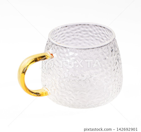 Clear textured glass mug with golden handle on white background, shallow depth of field, modern minimalist style Clear textured glass mug with golden handle on white background, shallow depth of field, modern minimalist style 142692901
