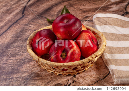 Flat nectarines in woven basket on rustic wooden surface with striped cloth, rich red and yellow tones, shallow depth of field Flat nectarines in woven basket on rustic wooden surface with striped cloth, rich red and yellow tones, shallow depth of field 142692904
