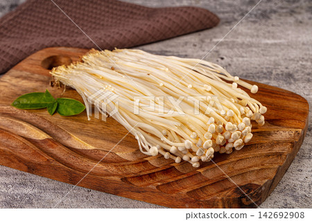 fresh enoki mushrooms on rustic wooden cutting board with green leaves, ready for asian cooking or gourmet meal preparation fresh enoki mushrooms on rustic wooden cutting board with green leaves, ready for asian cooking or gourmet meal preparation 142692908
