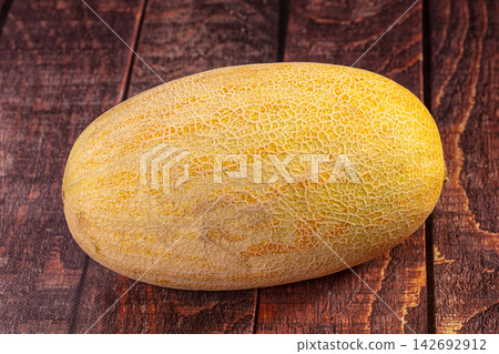 Ripe cantaloupe melon with netted rind resting on dark rustic wooden surface, warm natural lighting highlighting texture and golden yellow tones Ripe cantaloupe melon with netted rind resting on dark rustic wooden surface, warm natural lighting highlighting texture and golden yellow tones 142692912