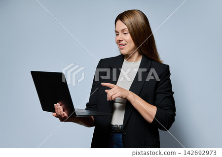 Businesswoman holding laptop and typing against grey background Businesswoman holding laptop and typing against grey background 142692973