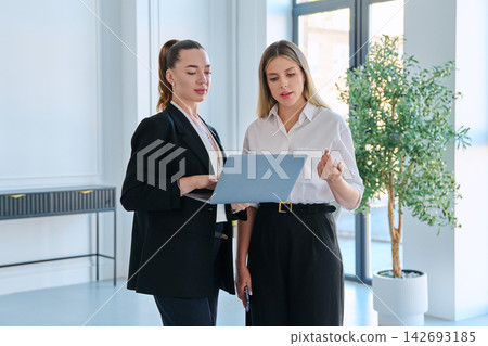 Two business women looking at laptop screen working together in bright office Two business women looking at laptop screen working together in bright office 142693185