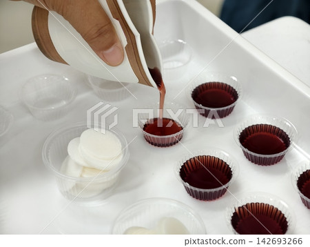 Close-up of preparing Holy Communion elements, pouring grape juice into cups alongside Communion wafers. Perfect for Christian church services, Easter, and religious concepts. Close-up of preparing Holy Communion elements, pouring grape juice into cups alongside Communion wafers. Perfect for Christian church services, Easter, and religious concepts. 142693266
