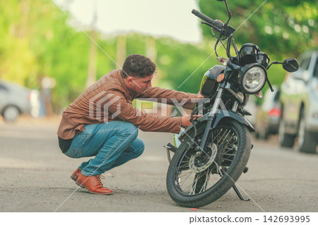 Biker repairing motorcycle on the road. Motocyclist fixing the motorcycle on the road, Man checking his motorcycle on the road Biker repairing motorcycle on the road. Motocyclist fixing the motorcycle on the road, Man checking his motorcycle on the road 142693995
