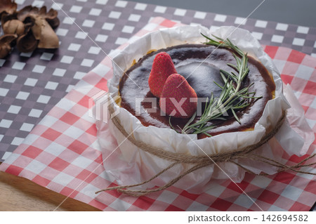 a basque burnt cheesecake topping with strawberry and rosemary serving on dish with crumpled paper 142694582