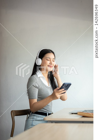 Young Asian woman closing eyes listening to music in headphones while sitting at table in a cafe. 142696349