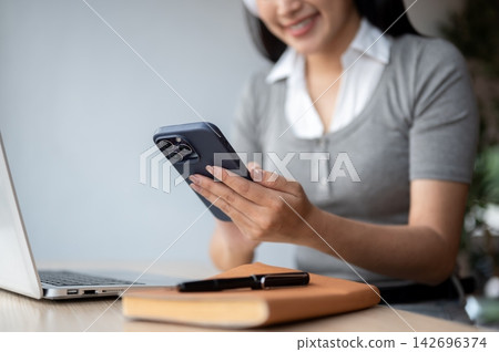 Asian Woman Holding Smartphone While Working On Laptop Asian Woman Holding Smartphone While Working On Laptop 142696374