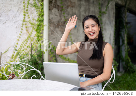 Cheerful Asian Woman Waving Hand In Video Call On Laptop Cheerful Asian Woman Waving Hand In Video Call On Laptop 142696568