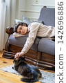 Tired young woman lying on sofa and gently petting beloved cat for emotional comfort at home 142696886