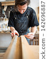 Carpenter making measurements for patch replacement on vintage wooden window frame in repair shop. 142696887