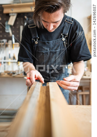 Carpenter making measurements for patch replacement on vintage wooden window frame in repair shop. Carpenter making measurements for patch replacement on vintage wooden window frame in repair shop. 142696887