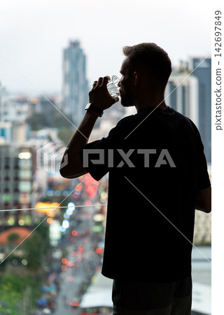 Man Drinking From Glass By Window Overlooking City. Alcohol Use, Loneliness And Coping With Emotional Stress Concept. Man Drinking From Glass By Window Overlooking City. Alcohol Use, Loneliness And Coping With Emotional Stress Concept. 142697849