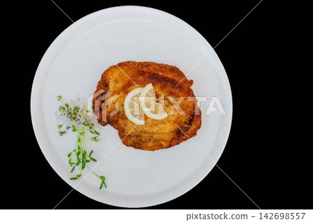 Golden fried schnitzel with lemon slices and sprouts on white plate Golden fried schnitzel with lemon slices and sprouts on white plate 142698557