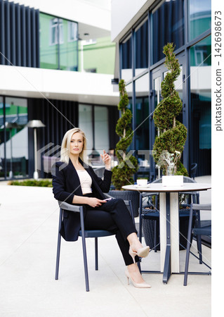 Blonde business lady looks at the phone, reading messages. Woman is relaxing in a cafe on the terrace enjoyment of life 142698673
