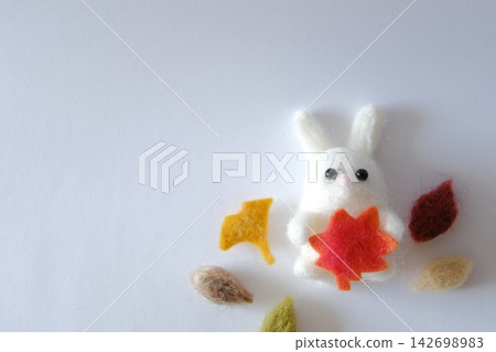 A white wool felt rabbit holding autumn leaves and autumn leaves A white wool felt rabbit holding autumn leaves and autumn leaves 142698983