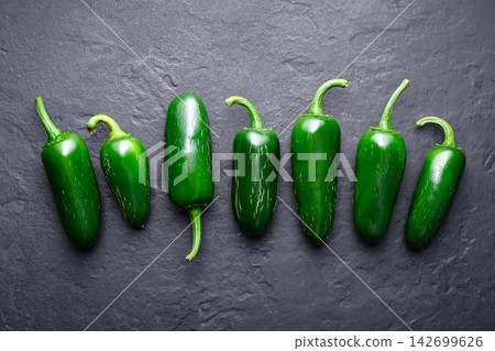 Row of jalapeno peppers on dark stone background Row of jalapeno peppers on dark stone background 142699626