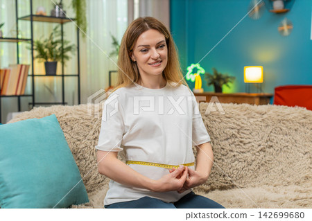 Pregnant woman measures belly with tape checks result smiles happy with nice growth on sofa at home Pregnant woman measures belly with tape checks result smiles happy with nice growth on sofa at home 142699680
