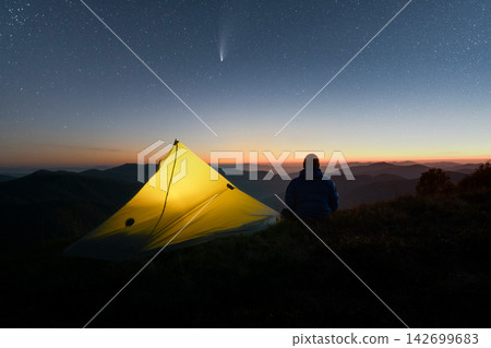 Yellow tent and hiker resting on a mountain ridge Yellow tent and hiker resting on a mountain ridge 142699683