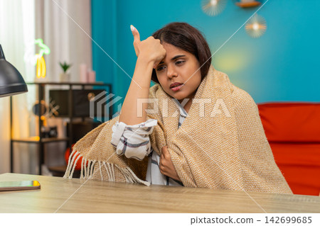 Indian woman wrapped in blanket touches forehead checking temperature feeling worried fever indoors 142699685