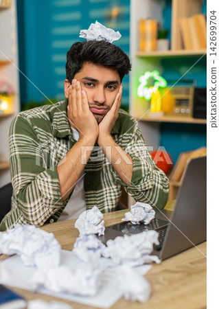Indian man on home table feeling frustrated with crumpled paper near laptop during hard remote work Indian man on home table feeling frustrated with crumpled paper near laptop during hard remote work 142699704