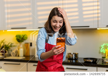 Young woman smiling using smartphone in home kitchen enjoying break during healthy meal prep routine Young woman smiling using smartphone in home kitchen enjoying break during healthy meal prep routine 142699735