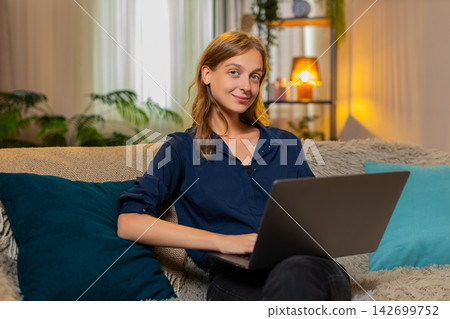Young woman on home sofa reads work message on laptop looking focused during remote business tasks Young woman on home sofa reads work message on laptop looking focused during remote business tasks 142699752