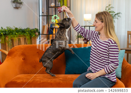 Middle-aged woman with dog plays tug of war rope ball pet resists pull woman guides gentle training Middle-aged woman with dog plays tug of war rope ball pet resists pull woman guides gentle training 142699833