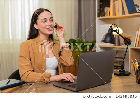 Young woman on home table working as call center operator on laptop answering client calmly online Young woman on home table working as call center operator on laptop answering client calmly online 142699839