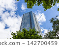 Low angle view of tall glass office tower framed by foliage 142700459