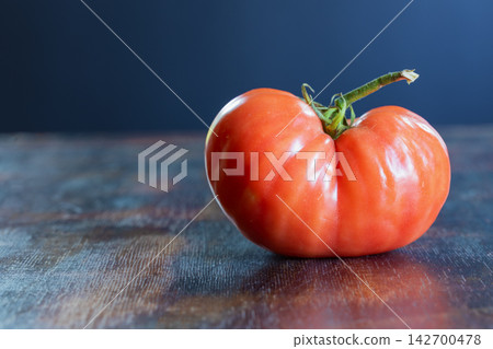 Close-up of ugly, naturally misshapen tomato with unusual irregular shape and pronounced lobes, resting on rustic wooden surface. Concept of accepting imperfect food, agricultural diversity Close-up of ugly, naturally misshapen tomato with unusual irregular shape and pronounced lobes, resting on rustic wooden surface. Concept of accepting imperfect food, agricultural diversity 142700478
