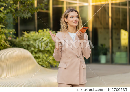 Young woman discussing work on speakerphone walking in city street with focused business expression Young woman discussing work on speakerphone walking in city street with focused business expression 142700585