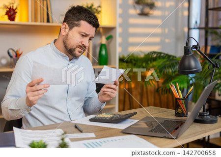 Young man on home table checking bills and reacting to unexpected payments with frustration stress Young man on home table checking bills and reacting to unexpected payments with frustration stress 142700658