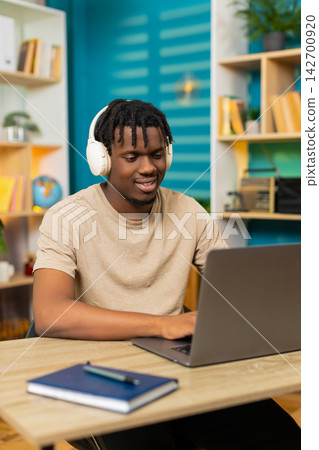 African American young man on home table in headphones working on laptop listening to music for work 142700920