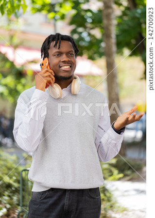 African American young man getting surprise smartphone call walking in city street during park walk African American young man getting surprise smartphone call walking in city street during park walk 142700923