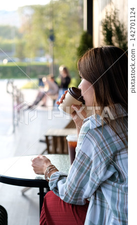 Woman Drinking Takeaway Coffee at an Outdoor Cafe Table with Green Park View in the Background Woman Drinking Takeaway Coffee at an Outdoor Cafe Table with Green Park View in the Background 142701124