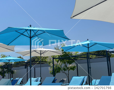 Rows of blue sunbeds and patio umbrellas under a clear summer sky at resort Rows of blue sunbeds and patio umbrellas under a clear summer sky at resort 142701798