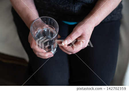 Senior woman holding medication pill and glass of water Senior woman holding medication pill and glass of water 142702359