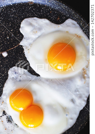 Two sunny-side up eggs frying in a nonstick pan Two sunny-side up eggs frying in a nonstick pan 142702371
