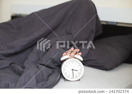 Woman's hand hitting snooze button on alarm clock Woman's hand hitting snooze button on alarm clock 142702374