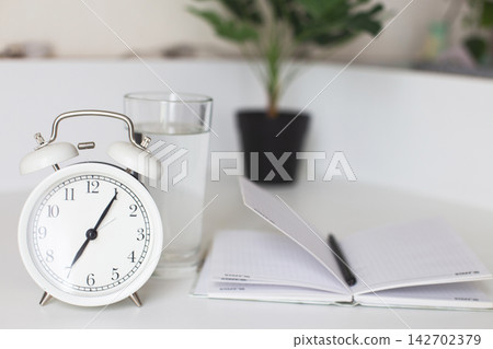 Alarm clock with water and notebook for morning routine Alarm clock with water and notebook for morning routine 142702379