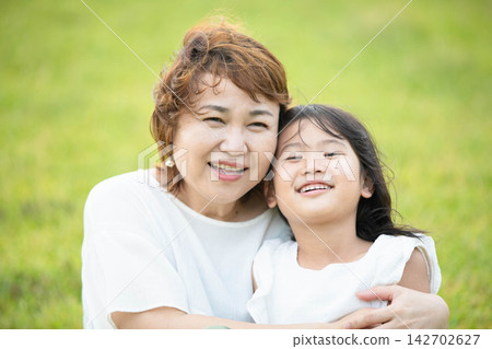 A smiling mother and child embracing on the park's lawn. A smiling mother and child embracing on the park's lawn. 142702627