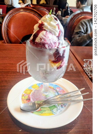 A parfait with berry sauce placed on a coffee shop table. A parfait with berry sauce placed on a coffee shop table. 142702706