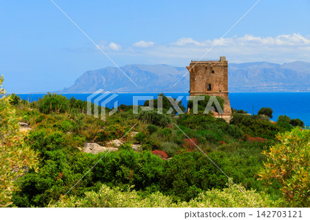 Ancient stone watchtower perched on a verdant hill overlooking the sparkling blue sea 142703121