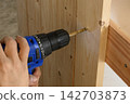 Carpenter using a power screwdriver to tighten a screw on wooden furniture 142703873