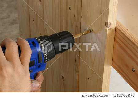 Carpenter using a power screwdriver to tighten a screw on wooden furniture Carpenter using a power screwdriver to tighten a screw on wooden furniture 142703873