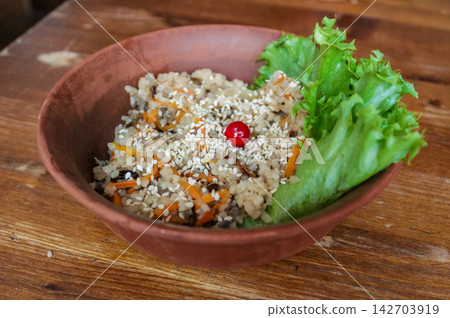 A bowl of rice salad displayed on a wooden table in a rustic interior creates a feeling of freshness and health. A bowl of rice salad displayed on a wooden table in a rustic interior creates a feeling of freshness and health. 142703919